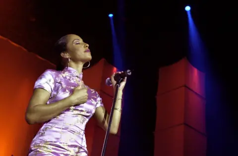 Getty Images Sade pictured performing on stage in 2023, she is wearing a silk light purple dress