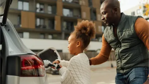 Getty Images Close-up of father with his daughter charging their electric car during autumn day