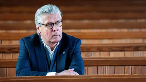 PA Media Malcolm Offord sitting on a church pew with his arms folded on top of the pew in front of him.