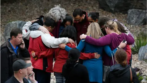 The Denver Post via Getty Images A group hugs one another as they wait to pick up their children after the shooting
