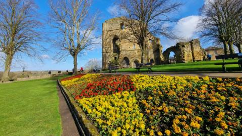 Blue skies above a ruined castle surrounded by lush green grass and colourful spring flowers