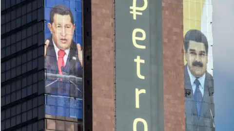 Getty Images The logo of the 'Petro' is displayed next to images of former Venezuelan president Hugo Chavez and current President Nicolas Maduro on a building in Caracas