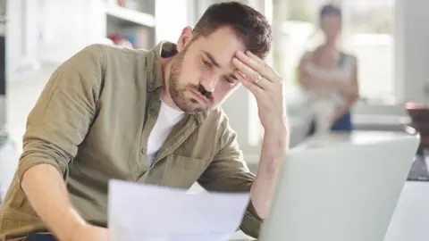 Getty Images Man worries about finances looking at bills