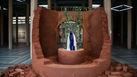 Annika Hammerschlag A statue of a person coloured blue, with a backdrop of brown brick surrounding them.