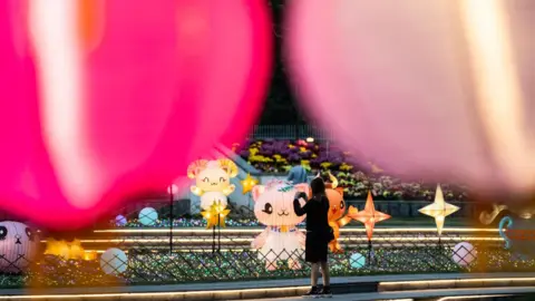 Hou Yu/China News Service/VCG /Getty Images A woman takes pictures of colourful lanterns set up at Hong Kong Velodrome Park