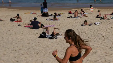 EPA Jogger runs down Bondi Beach past groups sunbathing on the sand