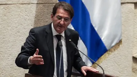 Boaz Bismuth/X Israeli MP Boaz Bismuth speaking into a microphone in front of a blue and white flag