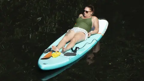 PA Media A paddle boarder enjoys the hot weather on the River Nidd in Knaresborough, North Yorkshire