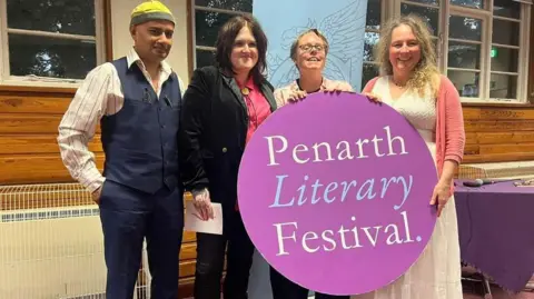 Rhian Elizabeth  Rhian Elizabeth with three other people at the Penarth Literary Festival, holding a banner with the event's name