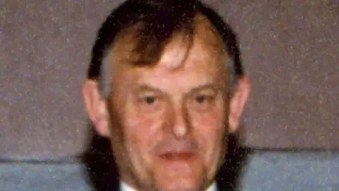 An old image of Sean Brown - a brown haired man with grey sideburns looking into the camera