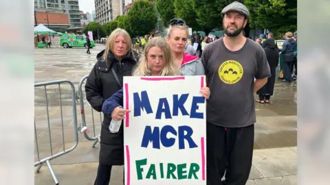 A group of three women and one man are protesting outside Manchester Central. A woman at the front of the group is holding a banner which says "make MCR fairer".