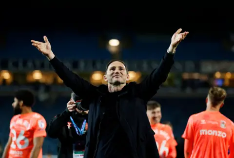PA Media Frank Lampard faces the fans with arms aloft. Coventry City players in orange away shirts can be seen in the background.