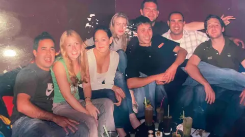 Jobe Ferguson A group of young men and women are smiling as they sit close to each other in a bar. 