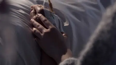 Getty Images A woman's hand holding another's in a hospital bed