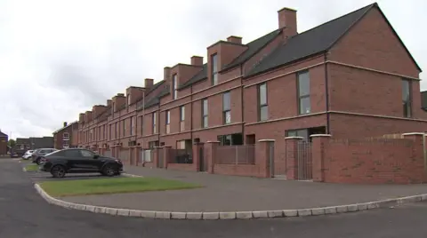 The picture shows a bloc of newly built terrace homes in north Belfast, some of which have windows boarded up