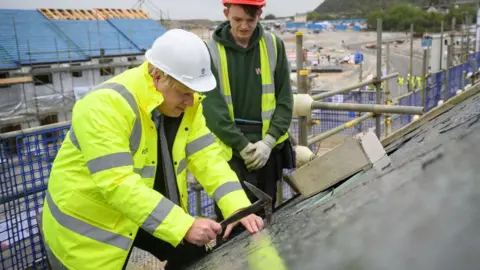 Getty Images Boris Johnson is shown how to fit roofing tiles