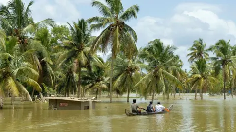 AFP Three people riding a boat through a flooded area