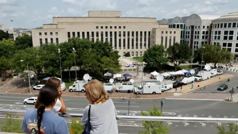 Reuters Tourists atop the National Gallery of Art look out over the news trucks in front of the federal courthouse where former U.S. President and Republican presidential candidate Donald Trump is expected to answer charges after a grand jury returned an indictment of Trump in the special counsel's investigation of efforts to overturn his 2020 election defeat In Washington, U.S. August 2, 2023.