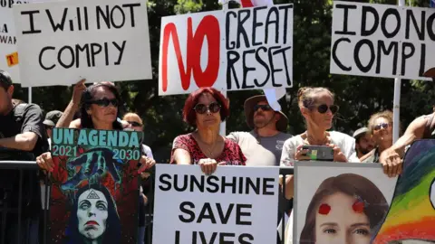 Getty Images People hold placards protesting the United Nations and the "great reset" at a rally of conspiracy theorists and supporters of US President Donald Trump on January 14, 2021 in Wellington, New Zealand