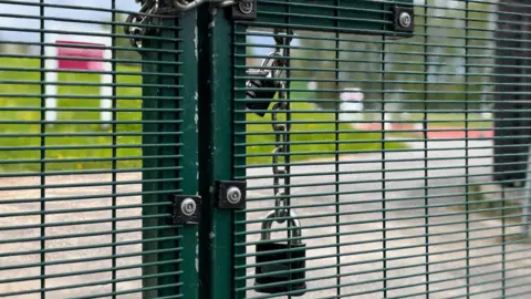 Simon Thake A green fence padlocked shut with an athletics track in the background