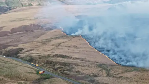 Gazz Hall An aerial view showing a large expanse of moorland with smoke rising from the ground and orange flames around a section of blackened land