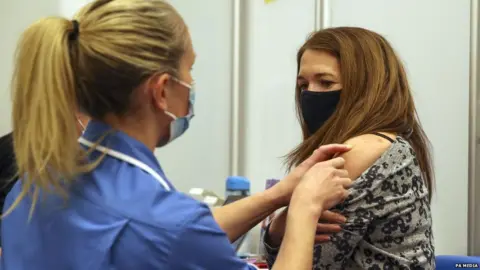 PA Media Caroline Nicolls receiving a Covid-19 vaccine, administered by nurse Amy Nash, at the Madejski Stadium in Reading