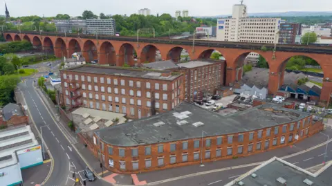 Marketing Stockport/Stockport MDC An artists' impression of brick tower blocks built under a brown brick bridge in a town centre