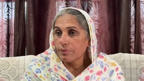 Pardeep Sharma/BBC Gurdeep Kaur, Amritpal Singh's mother, is seen sitting on a sofa with a printed scarf over her head.