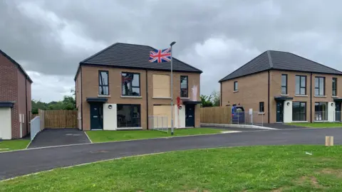 BBC An image of the damaged home alongside other homes in the estate. A Union Jack flag is flying on a lamppost outside the house. 