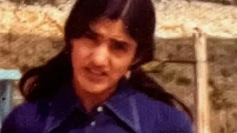 A woman in a blue-purple shirt outdoors in a vintage photograph.