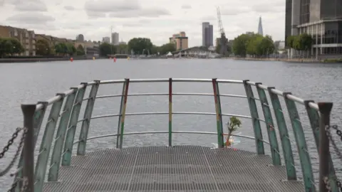 A dockland area with housing and boats at the quayside with flowers tied to the railing. 