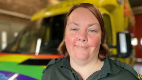 BBC Joanna Paskell in uniform, stood in front of an ambulance