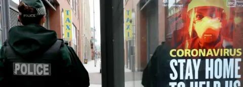 PA Media PSNI officer beside coronavirus advice poster