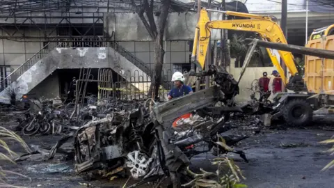 EPA An Indonesian officer inspects the scene of a bomb blast in front of a church in Surabaya, East Java, Indonesia, 13 May 2018