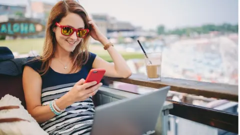 Getty Images Woman sat at a balcony with laptop and phone