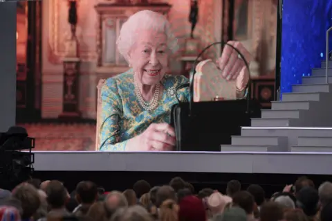 PA Media The Queen producing a marmalade sandwich from her handbag, seen on a big screen outside Buckingham Palace