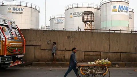 Getty Images A man pushes his cart as he walks past Bharat Petroleum's storage tankers in Mumbai on December 8, 2022.