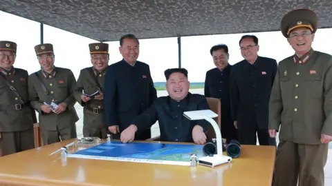 KCNA Kim Jong-un, seated in centre at a desk with a map, is seen surrounded by smiling officials and military personnel in an official photo