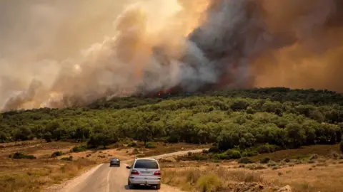 Getty Images Cars driving on road next to plumes of smoke