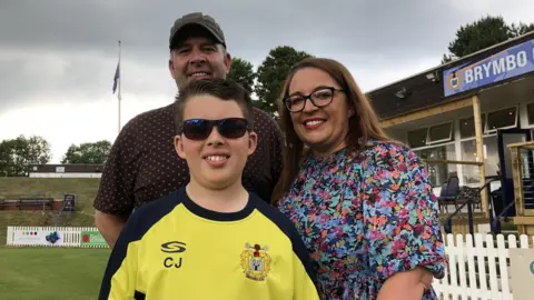 Charlie wearing his glasses with his parents at the Brymbo cricket ground