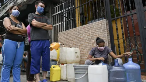 Getty Images A woman fills a water container from a hose in Petare in Caracas