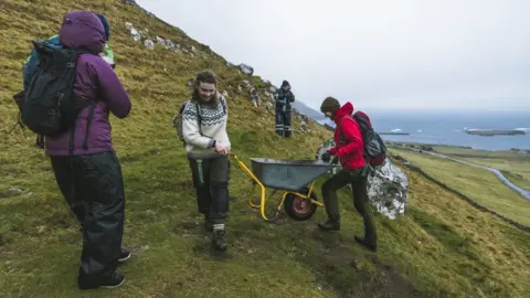 SAVIOUR MIFSUD Brown Group members help each other to push a wheelbarrow in the hills in Kirkjubøur