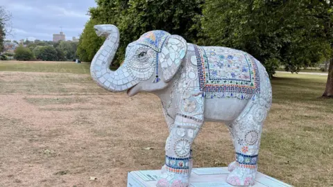 Thames Hospice A sculpture of an elephant with artistic designs around its body is pictured in a large green field in front of a row of trees.