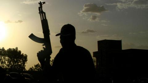 A silhouetted Sudanese fighter holds up a gun