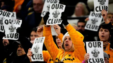 PA Media Fans holding up posters which say "Our club" with the football emblem on. 