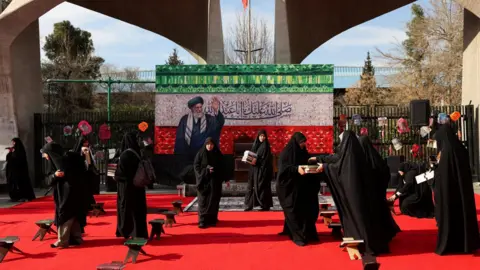 WANA/Via Reuters Women prepare a makeshift memorial in tribute to Iran's late Supreme Leader Ayatollah Ali Khamenei on a street in Tehran, Iran (4 March 2026)