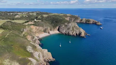 A picture taken from above, looking down on the island of Sark. There are a number of boats around the island, with sand beaches.