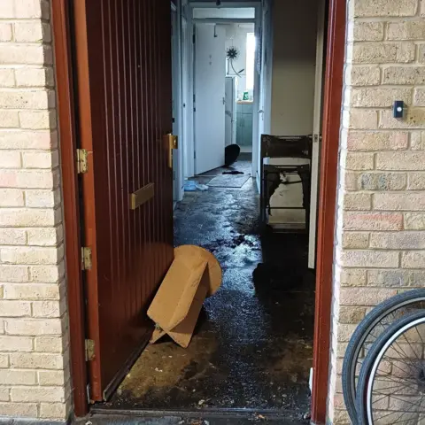 London Fire Brigade Wet hallway with wooden door and burnt furniture. Two bike wheels are to the right