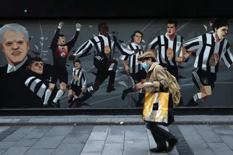 Reuters Man with mask walks past Newcastle United mural