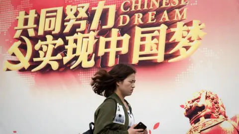 Getty Images A woman walks past a billboard promoting the "Chinese Dream", a slogan associated with Chinese president Xi Jinping, in Beijing